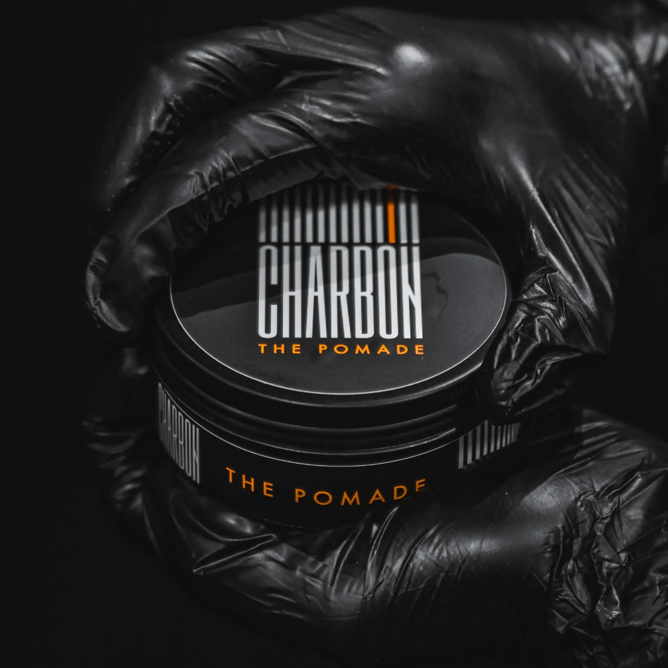 Un pot de pommade Charbon tenu par une main gantée de noir